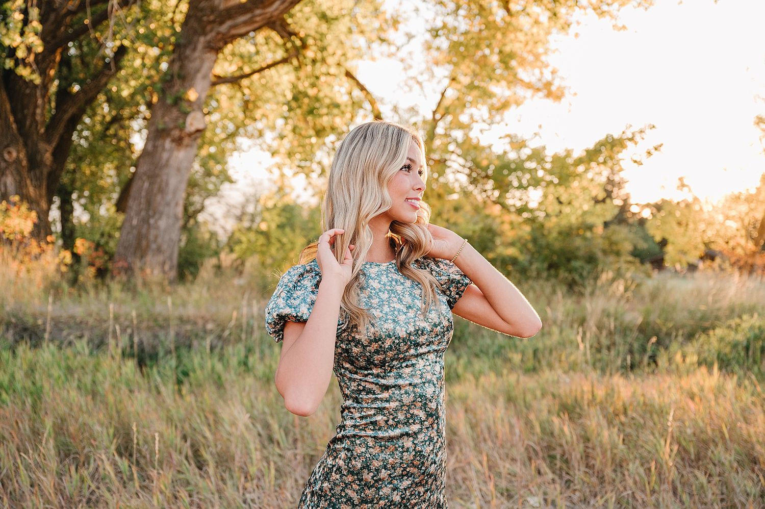 A figure in a floral dress poses in a field of tall grass during golden hour.