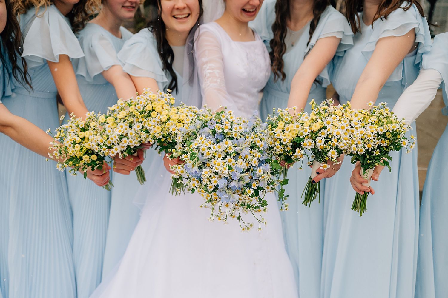 Bridesmaids in light blue dresses hold delicate bouquets of yellow and white flowers at a spring wedding.