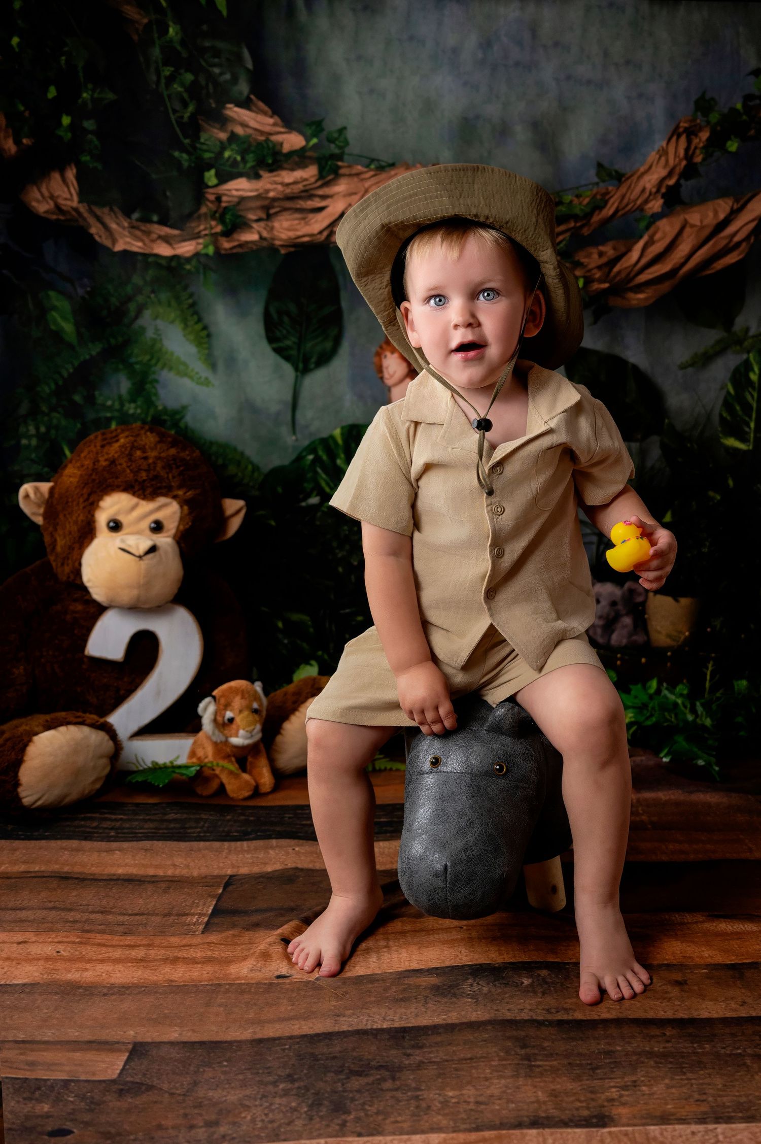 Baby in light blue overalls sits on white surface while painting with colorful paints and art supplies.