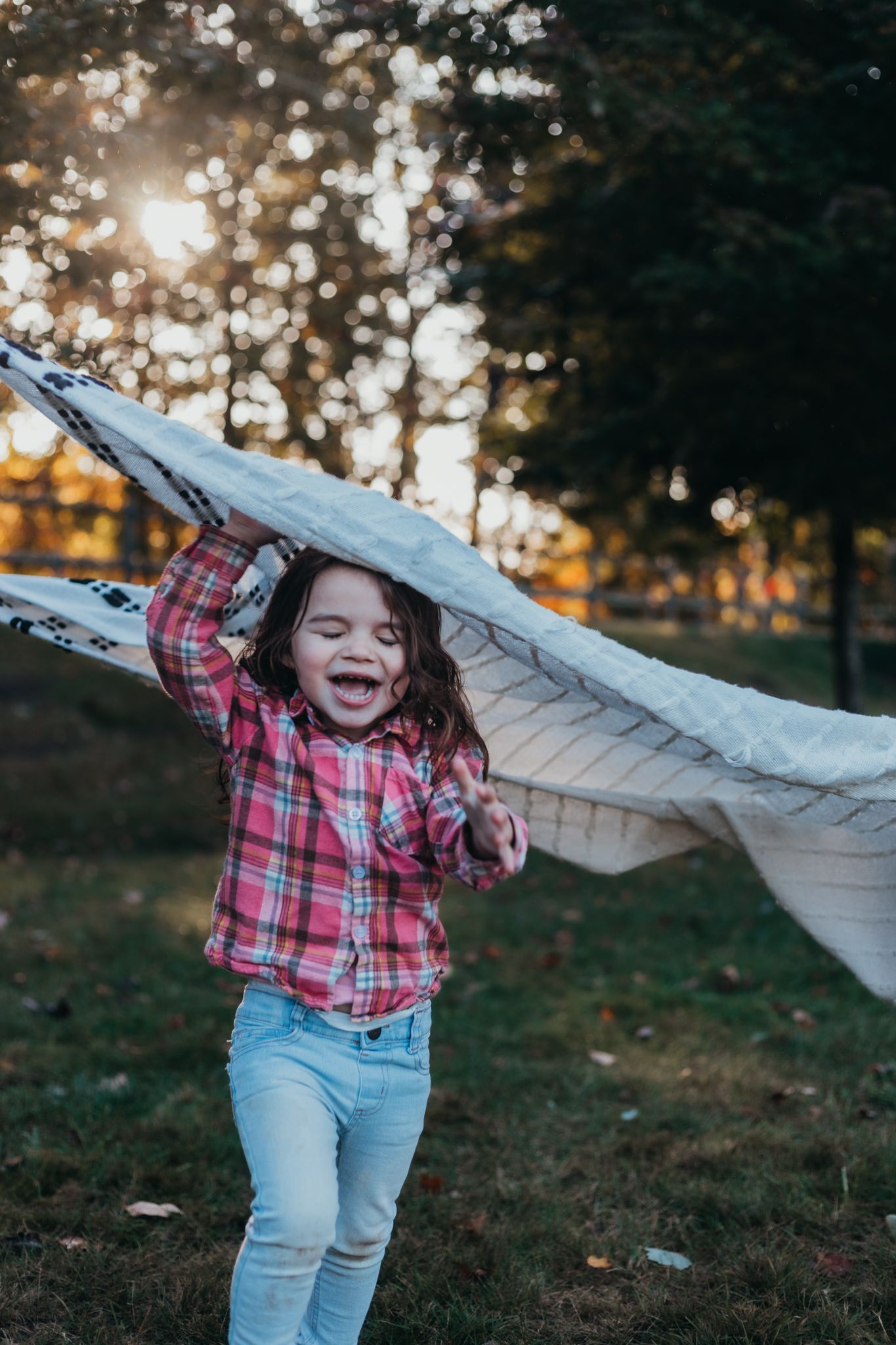 girl running under a blanket having fun under the sunset at a park with family
