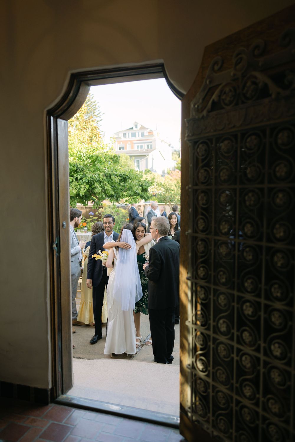 Wedding guests gather outside an ornate doorway with decorative metalwork as seen from inside a church entrance.