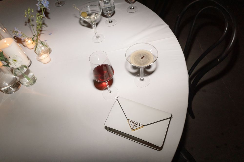 A white cocktail table with a glass of red wine and an elegant white purse in spotlight.
