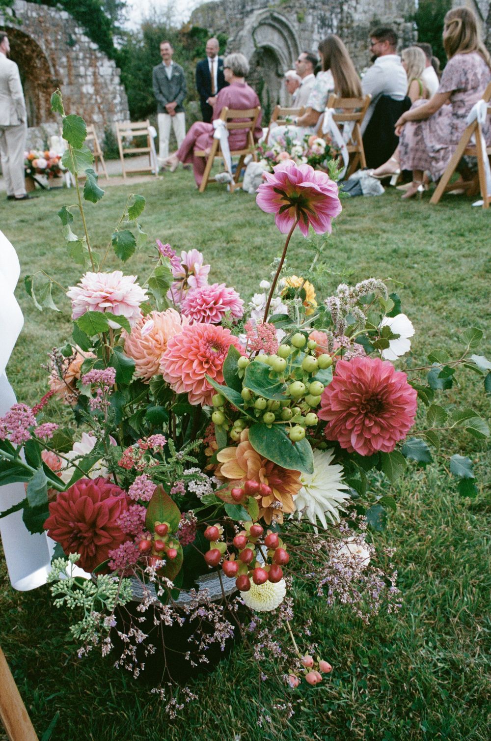 Beautiful pink and coral dahlias on 35mm film in outdoor floral arrangement with stone ruins and garden party setting in background.