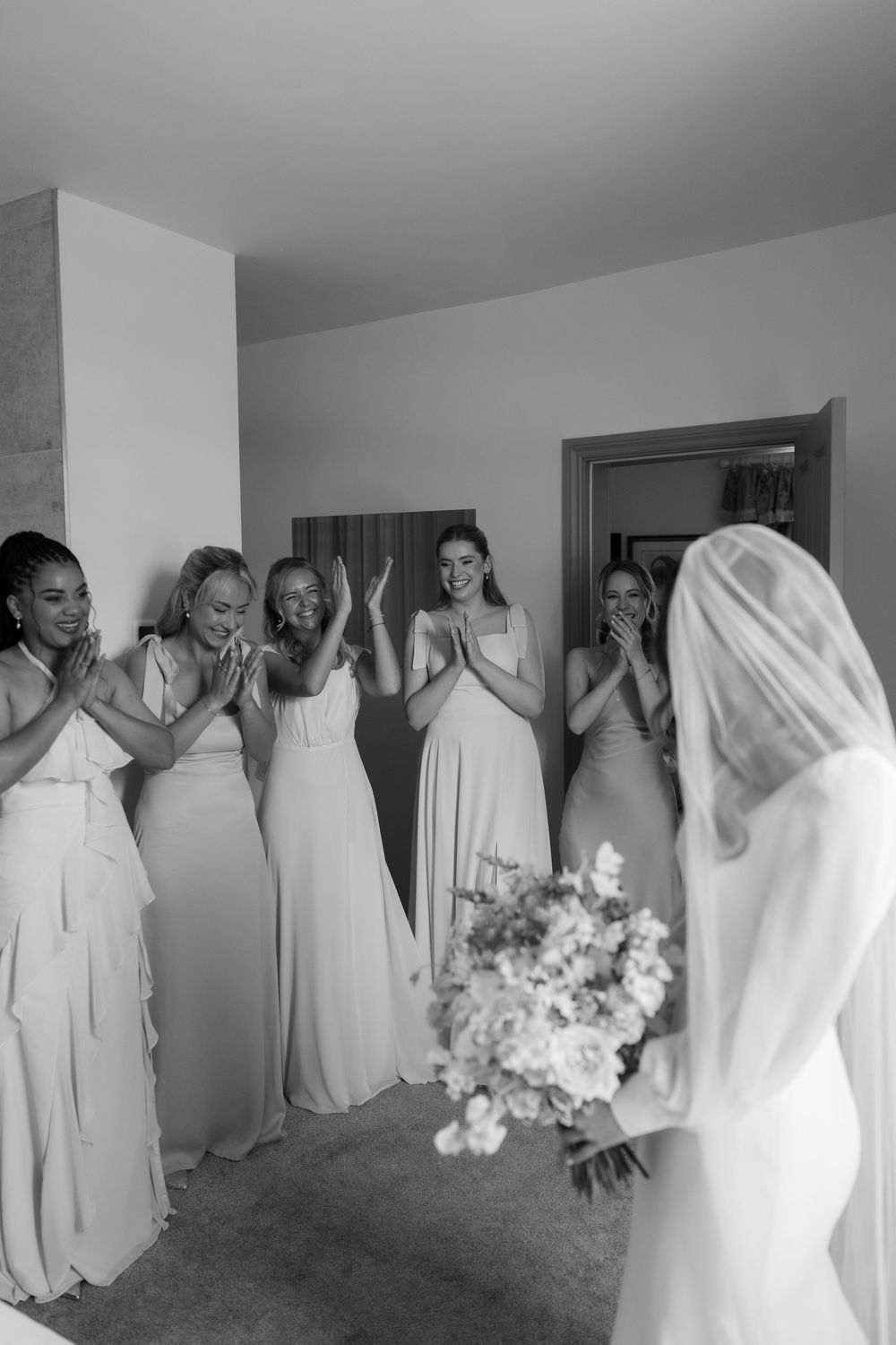A panoramic black and white photo of bridesmaids in matching white dresses lined up against a wall.