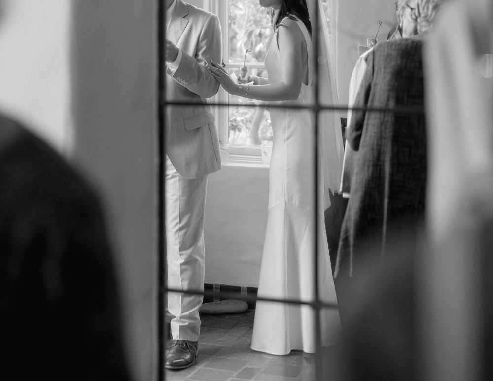 A black and white photo shows a partial view through window panes of people standing in formal attire.
