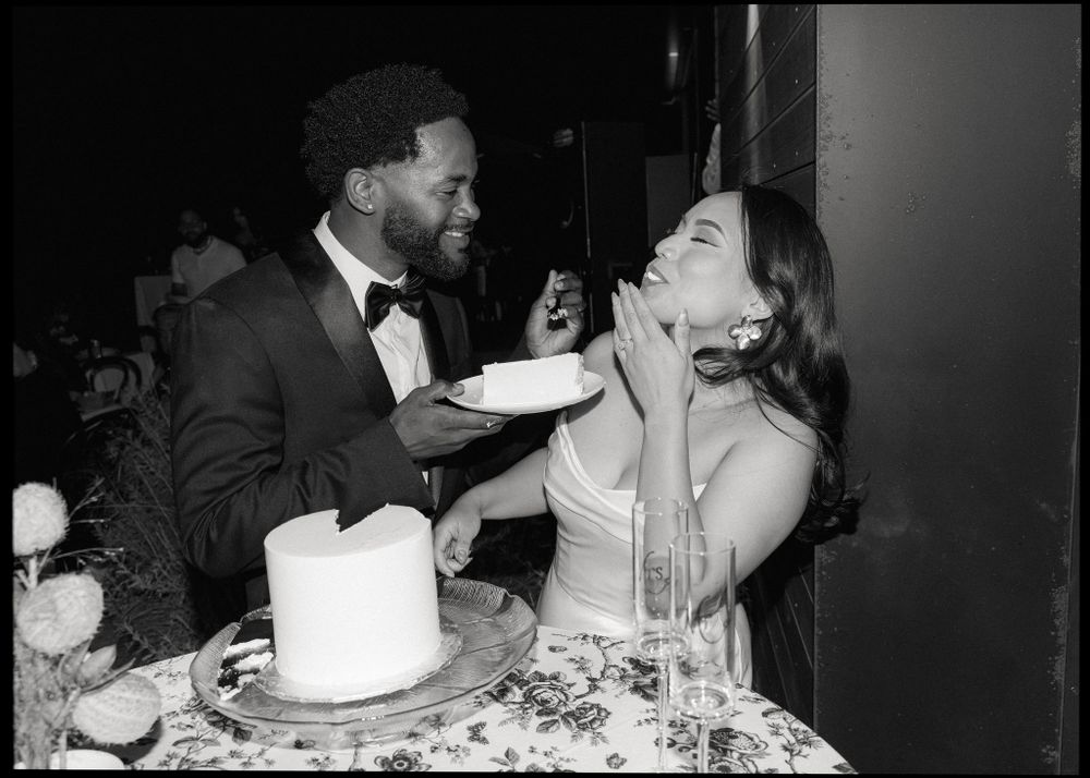 Two people sharing cake and laughing together at a formal event in black and white photography.