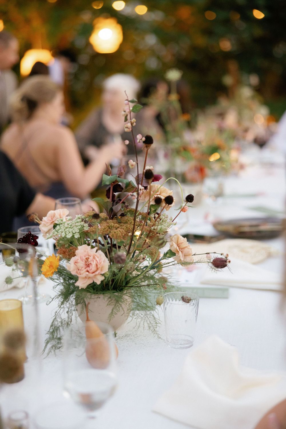 A romantic wedding reception table with blush roses and dried floral centerpiece under warm string lights.
