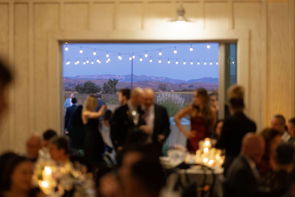 Blurred reception party scene with string lights and candlelit tables during an evening celebration.