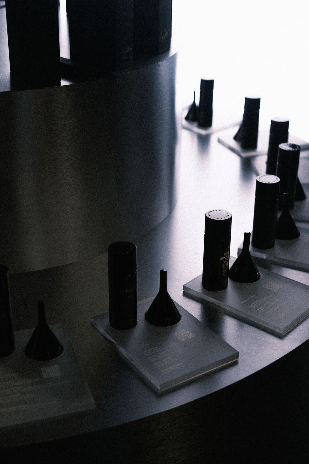 Dark perfume bottles displayed on metallic circular shelves in a dimly lit luxury fragrance boutique.