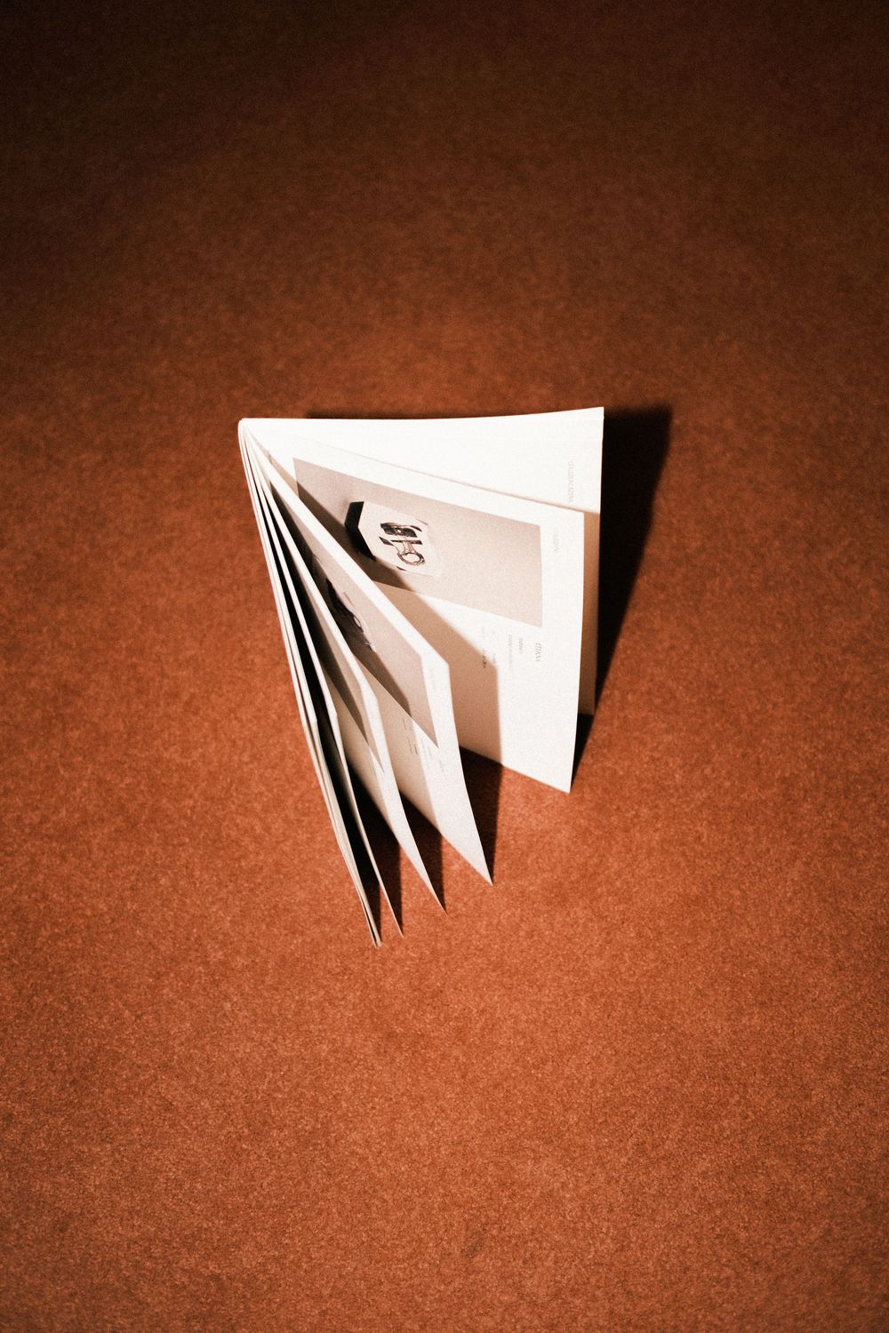 A small open booklet with black and white photos stands upright on a warm brown surface.