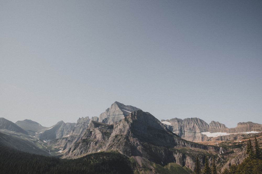 Majestic rocky mountain peaks rise against a pale blue sky in the wilderness.