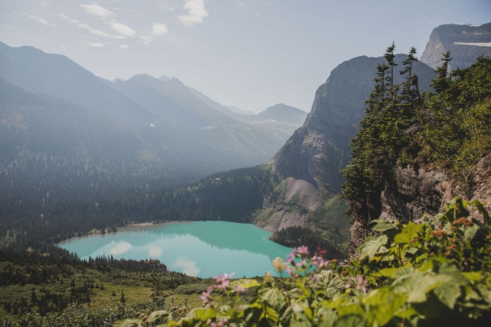 Stunning turquoise alpine lake viewed through pine trees with mountain backdrop.
