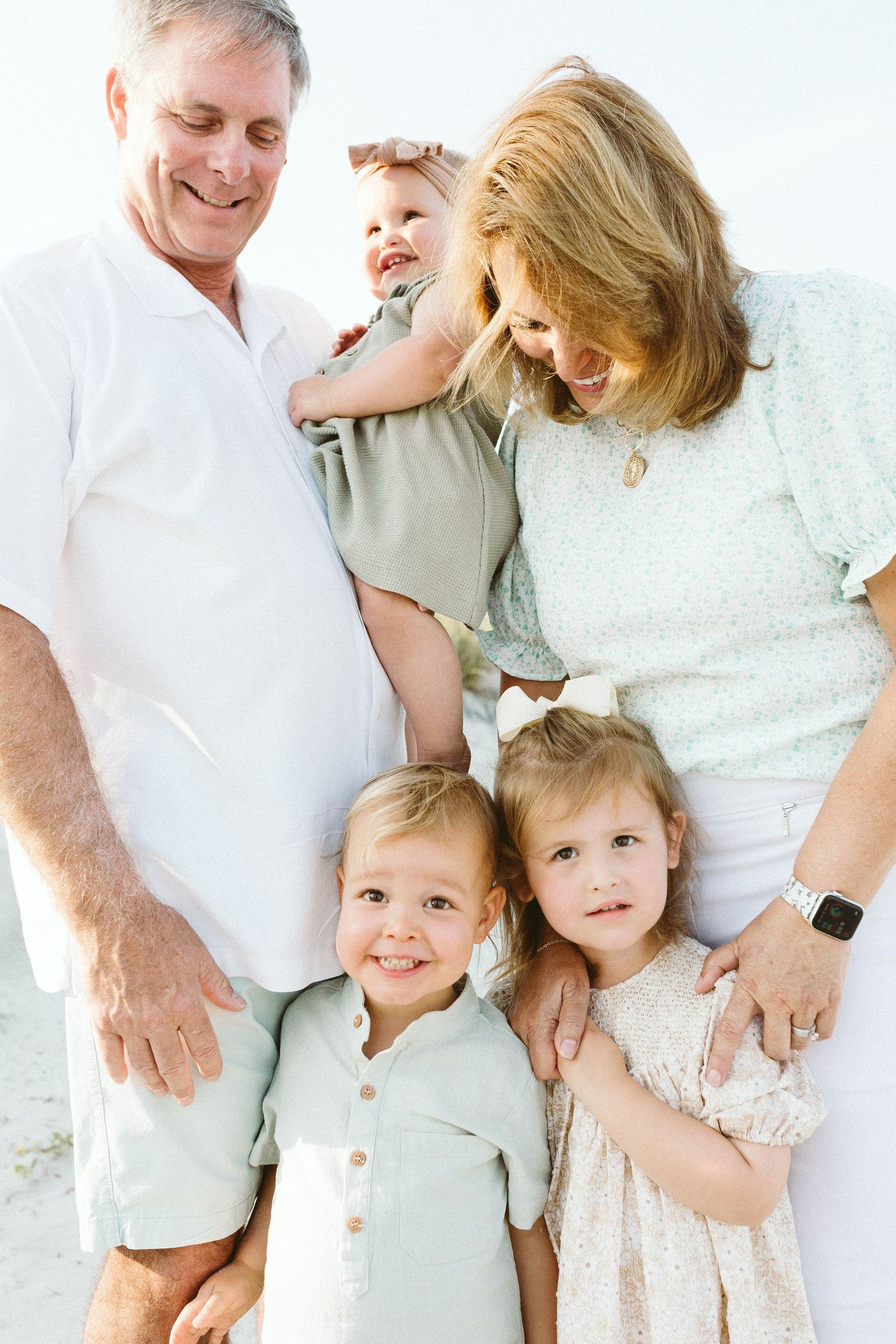 A family in white and neutral clothing shares joyful laughter during an outdoor photo session with B. Logsdon Photography.