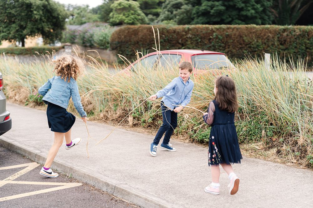 Children playing and running together on paved path surrounded by tall grass.