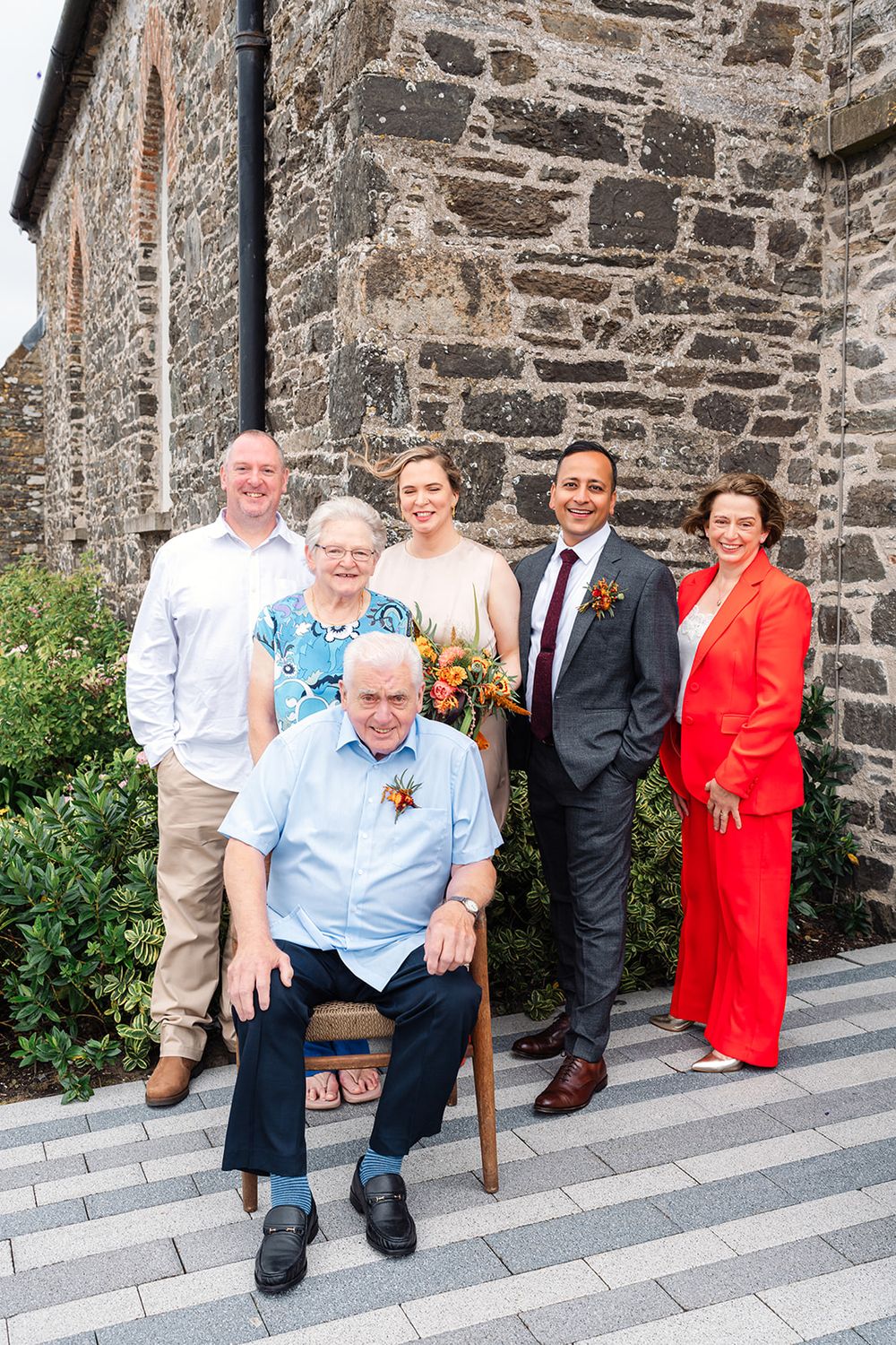 Group photo of wedding party gathered outside historic stone church building.