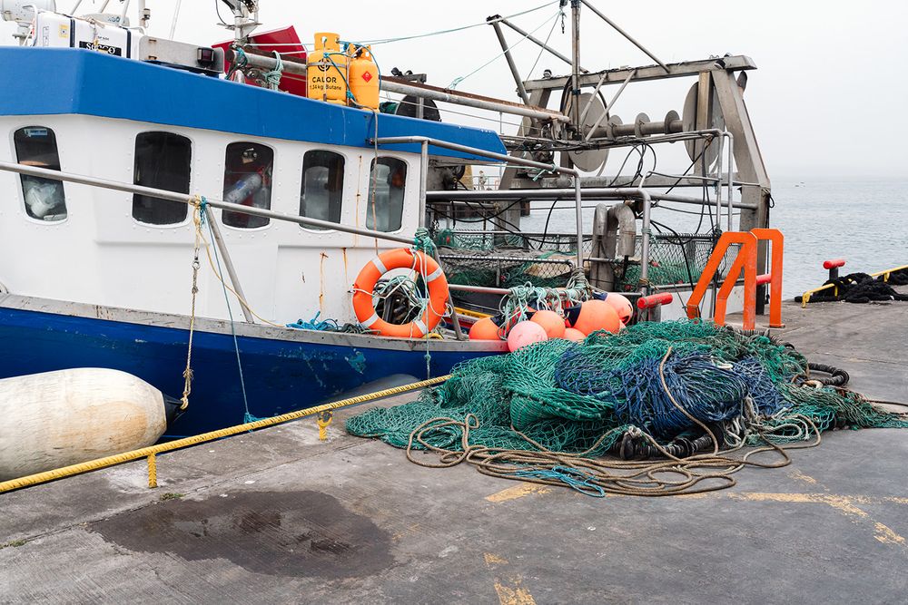 Blue fishing boat docked at harbor with green fishing nets and orange life preservers.
