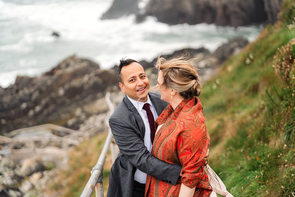 Joyful moment captured on coastal clifftop with dramatic ocean backdrop.