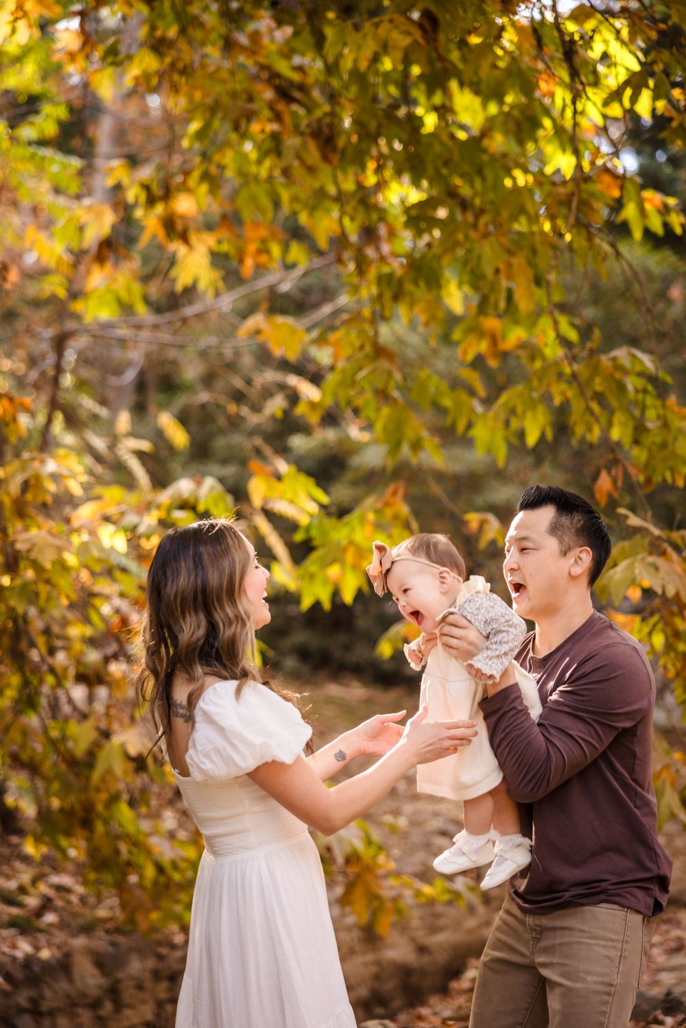 A joyful outdoor family moment captured during autumn with golden fall foliage in the background.