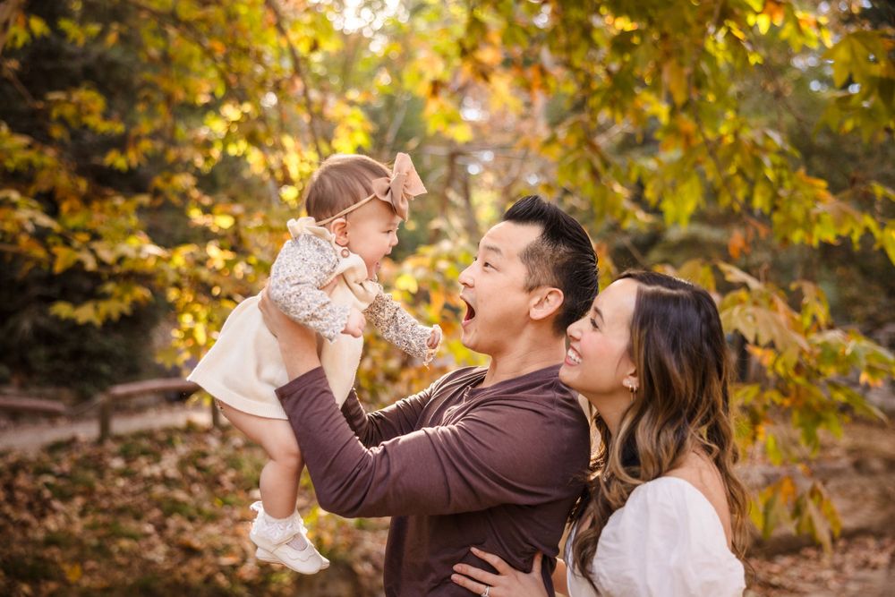 A family shares a joyful moment together outdoors surrounded by golden autumn foliage in a park setting.