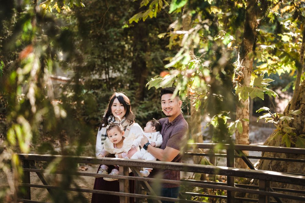 Family enjoying a peaceful moment together on a wooden bridge surrounded by sunlit trees in a forest setting.
