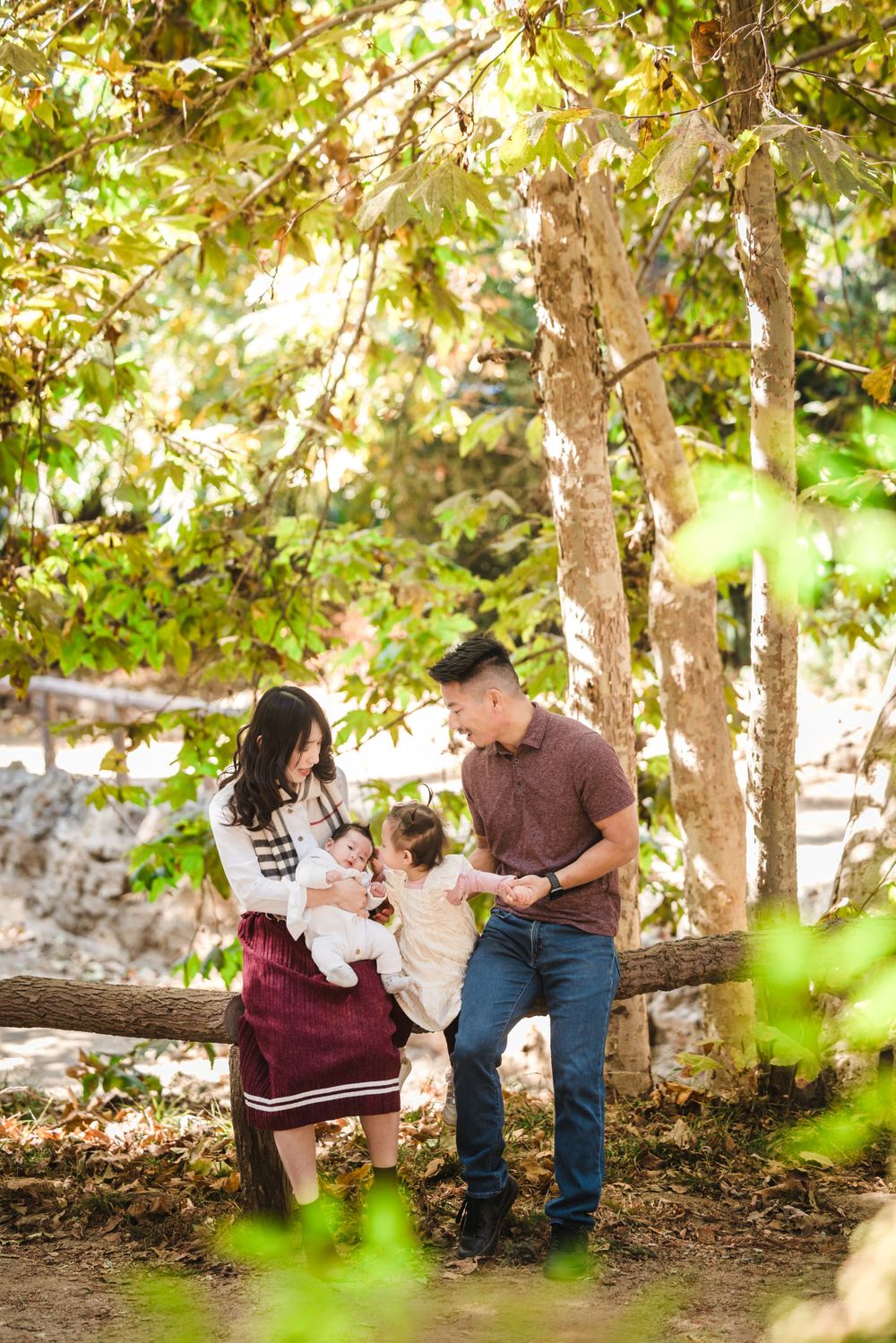 A group gathers on a wooden bench surrounded by sunlit trees in a peaceful forest setting on an autumn day.