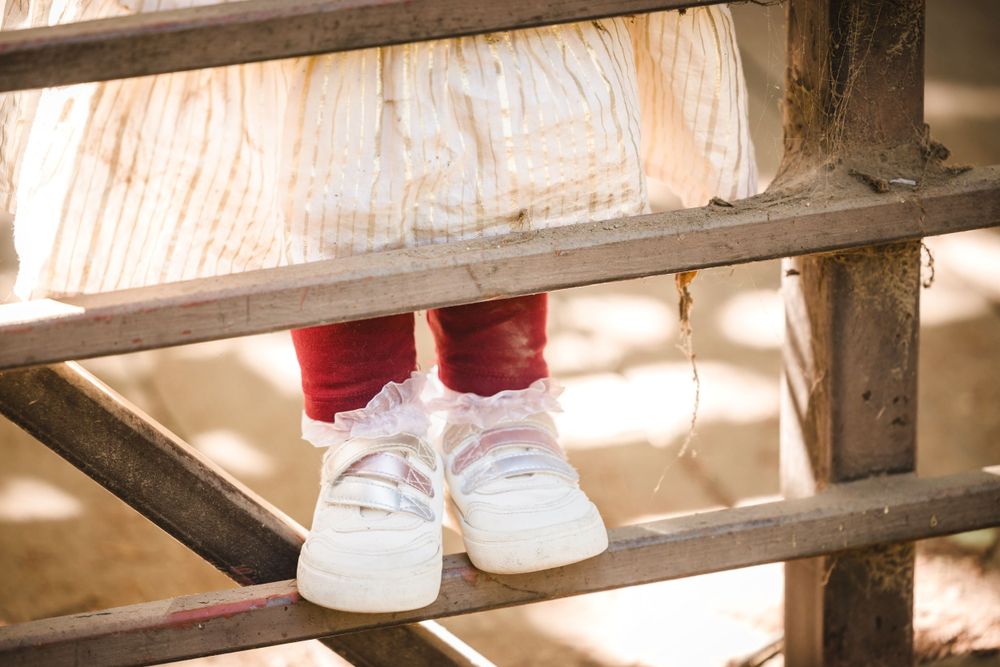 A person's feet in white sneakers and red socks standing on old wooden stairs with light shining through.