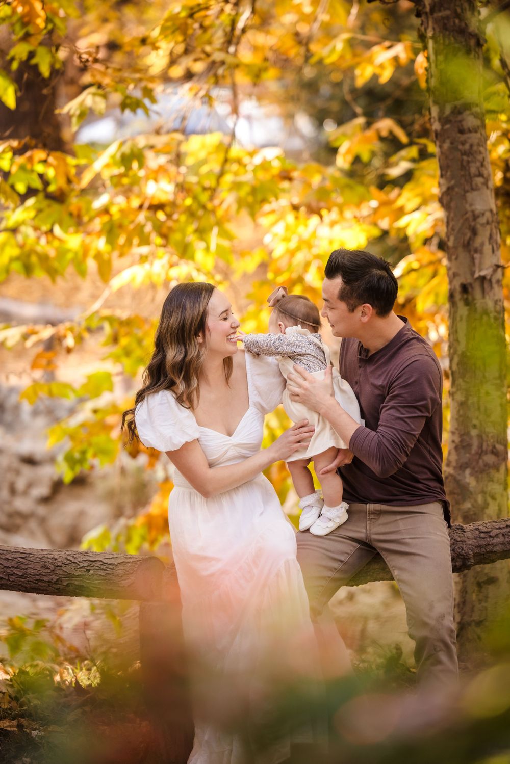 A loving family moment captured outdoors in autumn with golden fall foliage creating a warm, dreamy backdrop.