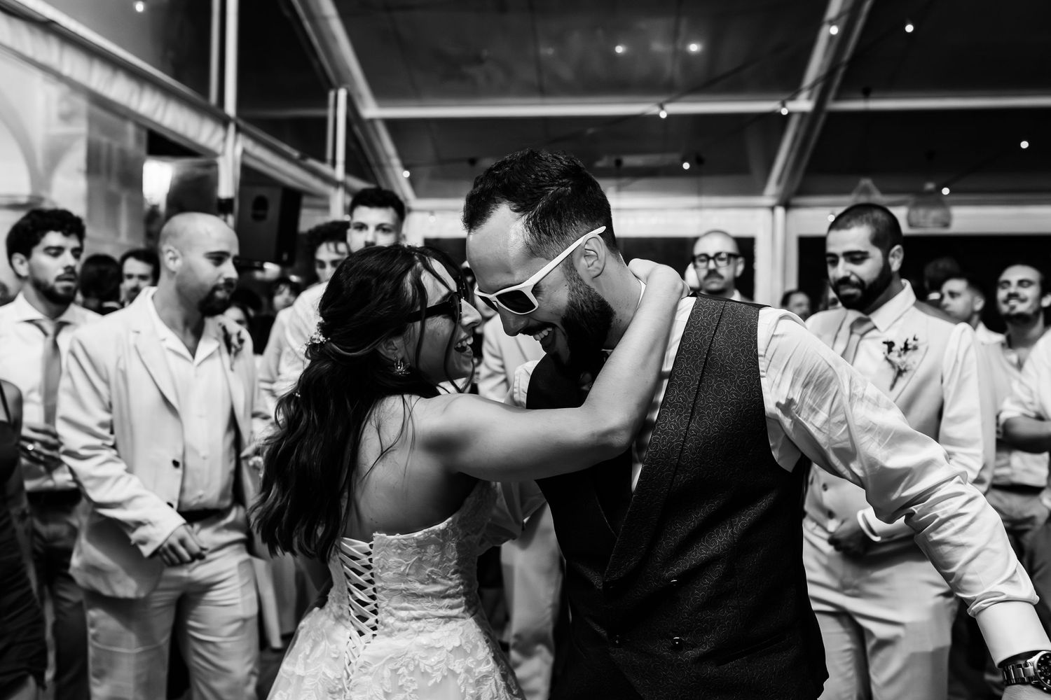 A loving couple embraces in a tender dance moment at an event while other guests can be seen in the background.
