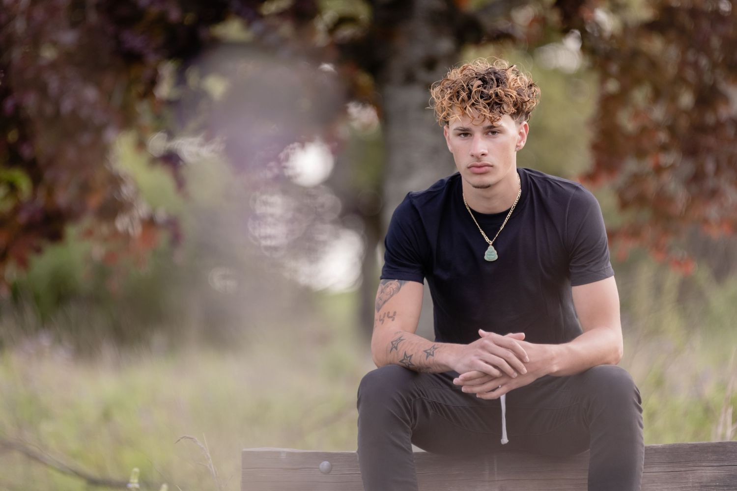 Portrait of someone in a black t-shirt sitting outdoors on a bench with blurred natural background.
