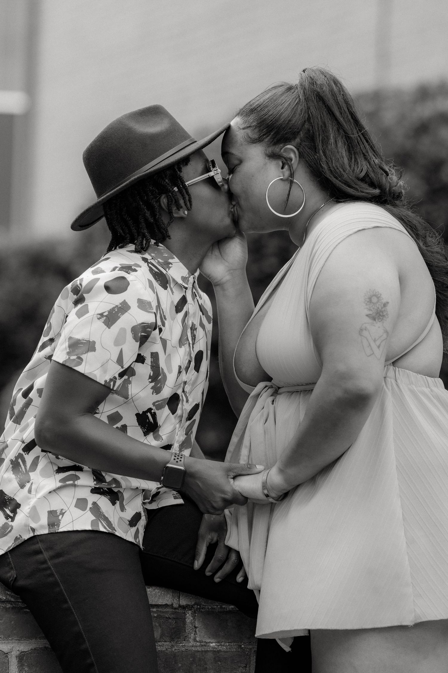A tender black and white portrait of a romantic couple sharing an intimate kiss while seated on a brick wall.