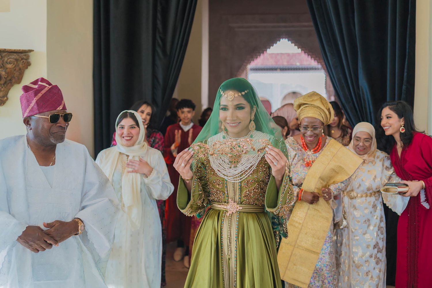 Joyful traditional wedding celebration showing guests in colorful formal attire and head coverings dancing together.