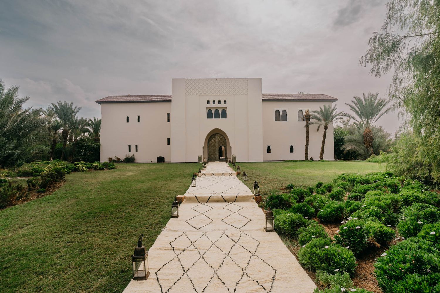 Elegant white Moroccan-style villa with arched entrance and geometric stone pathway through manicured gardens.
