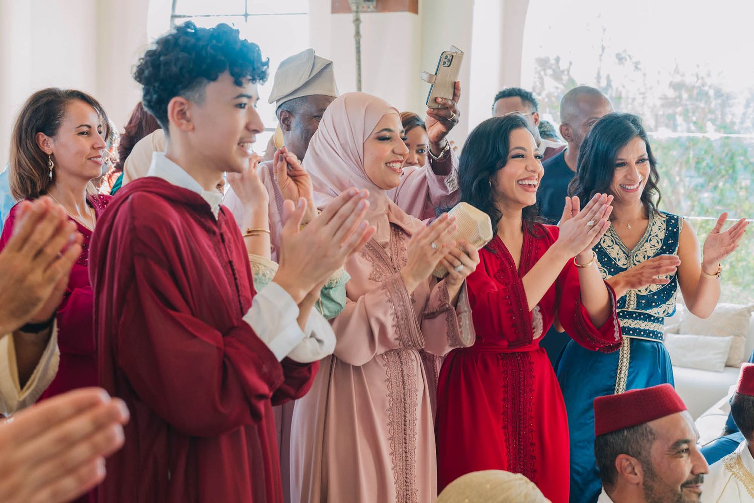 A diverse group of people clapping and celebrating together at an indoor gathering, wearing colorful attire.