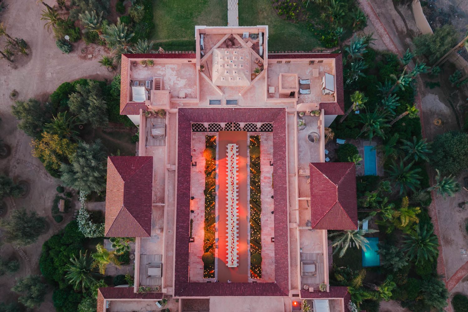 Aerial view of a red-tiled Buddhist temple with symmetrical layout and glowing lanterns illuminating the central courtyard.