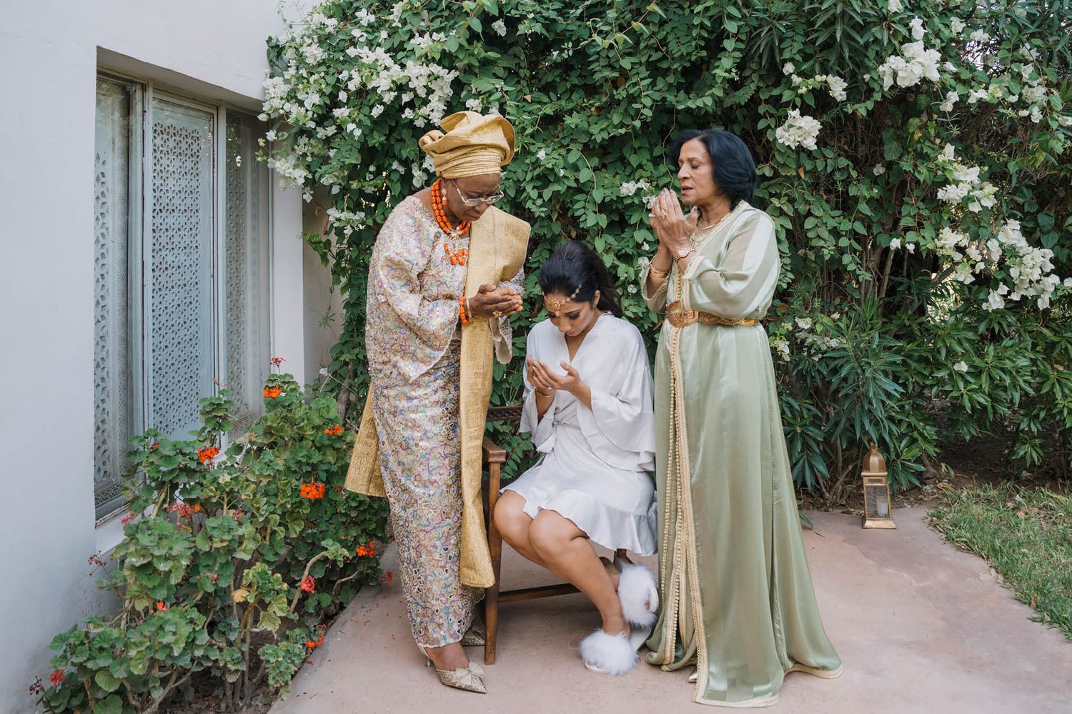 Three friends share a joyful moment in a garden with blooming roses, wearing elegant formal dresses in soft pastel colors.
