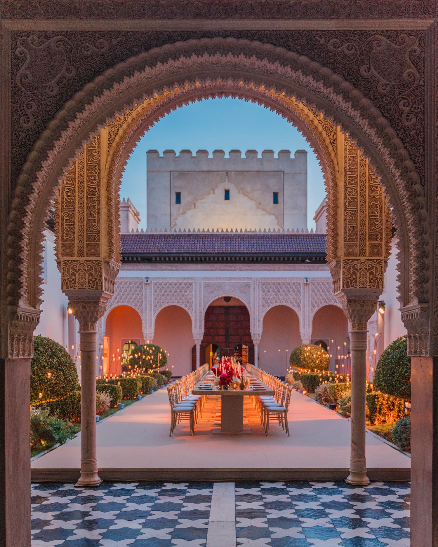 Luxurious Moroccan courtyard with ornate archways and dining setup framed by traditional Islamic architecture at sunset.