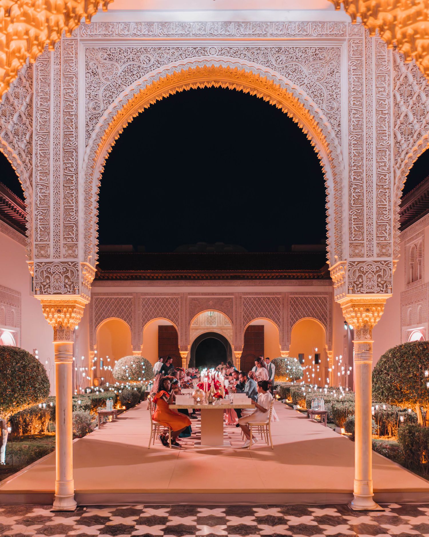 Ornate Moroccan-style archways frame an elegant outdoor dining setup with twinkling lights and decorative lanterns at night.