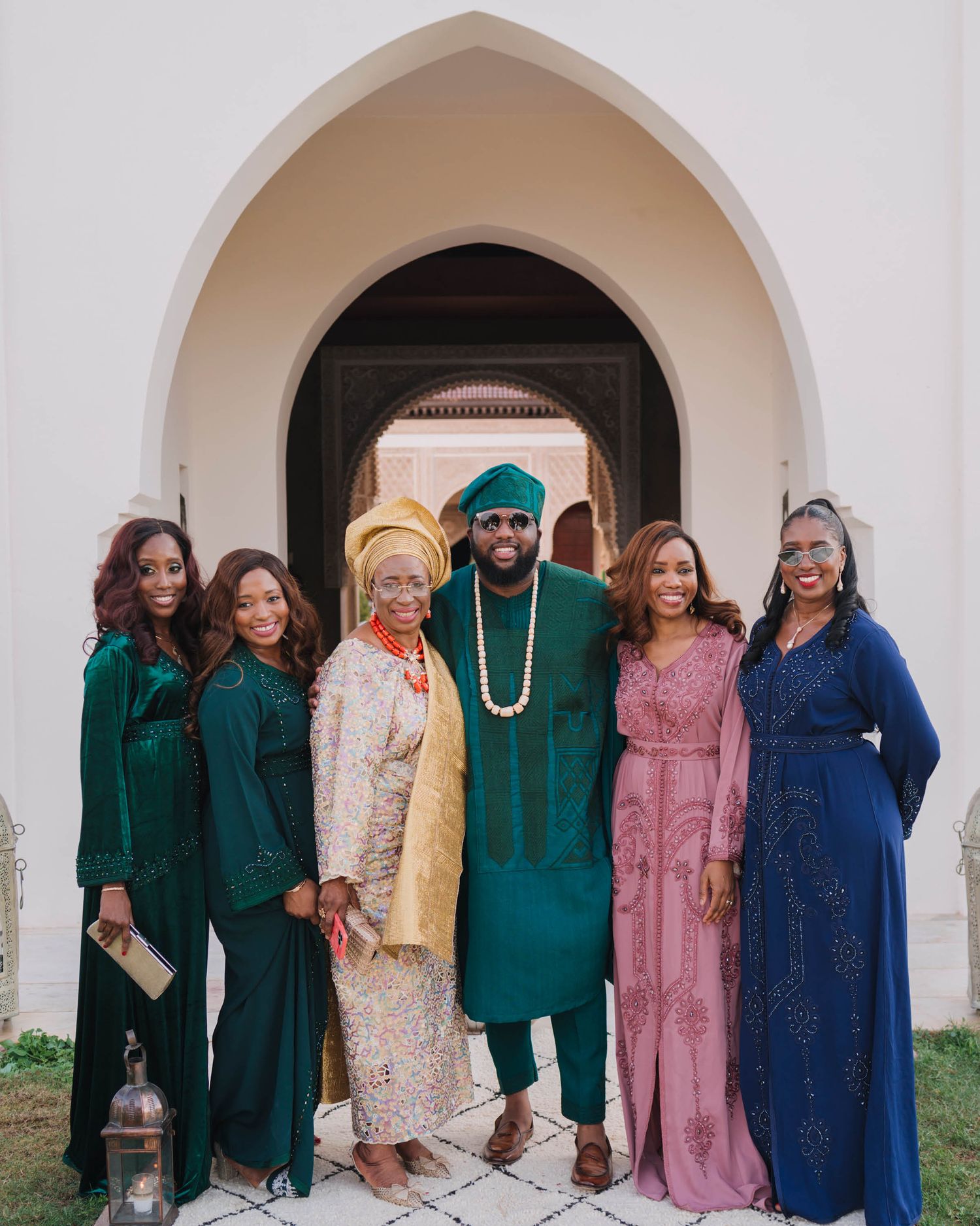Group in coordinated formal attire standing under arched doorway in jewel-toned dresses and traditional formal wear.