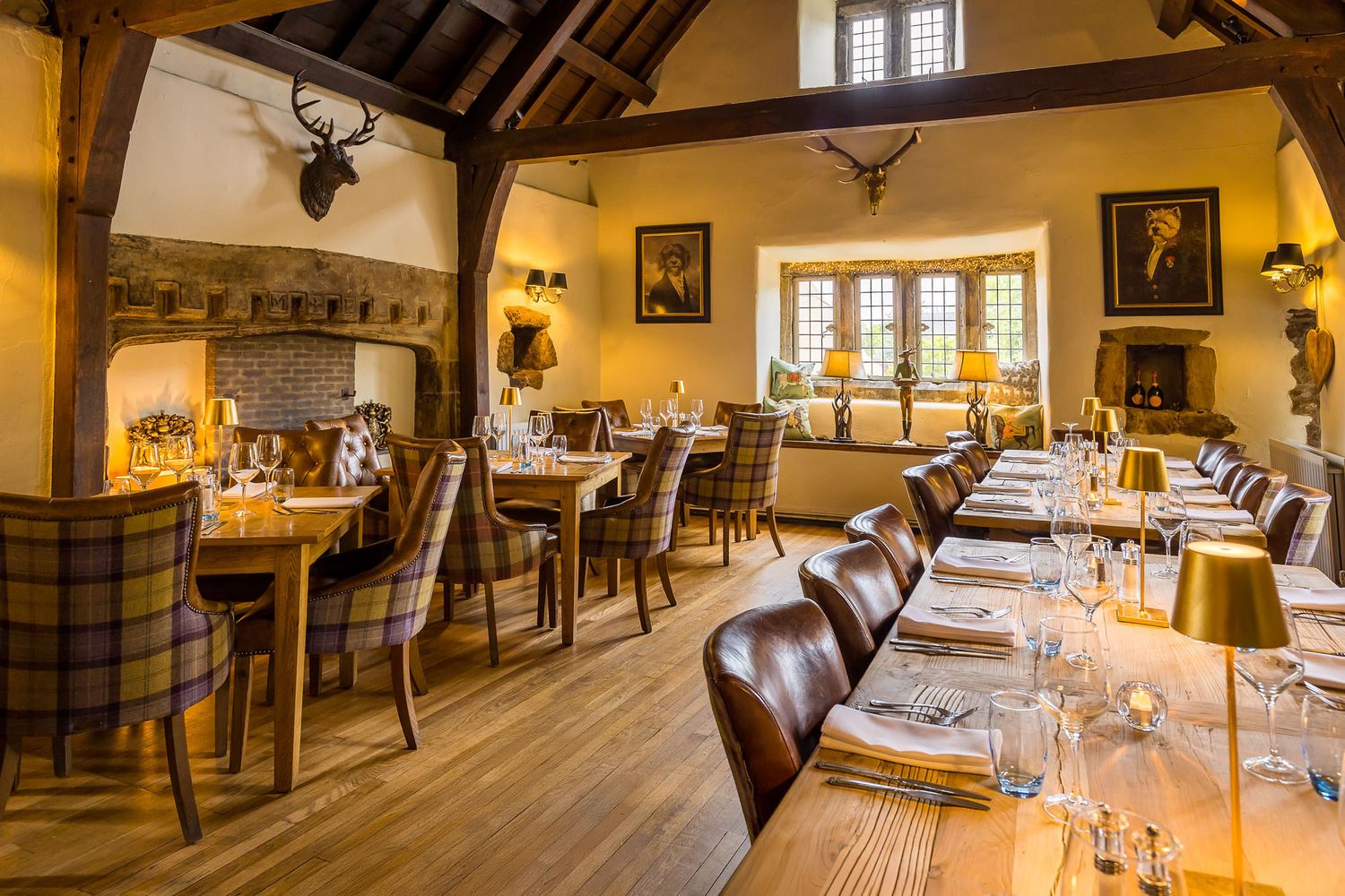 Charming dining room with rustic beams, leather and plaid seating, a cozy fireplace, and warm ambient lighting in a historic setting.