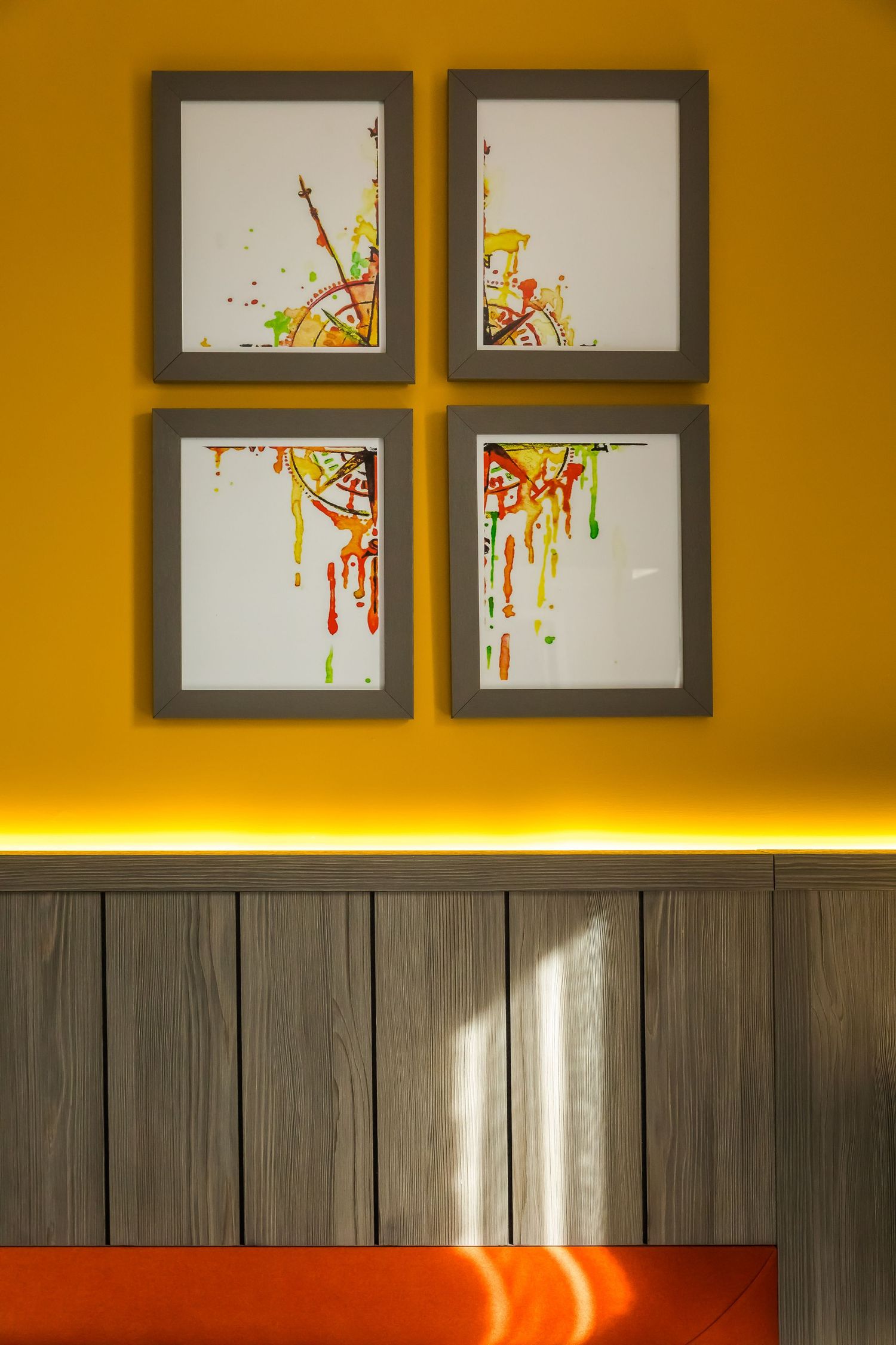 Framed abstract art on a bold yellow wall with warm lighting and wood panel detailing, creating a vibrant and modern interior feature.