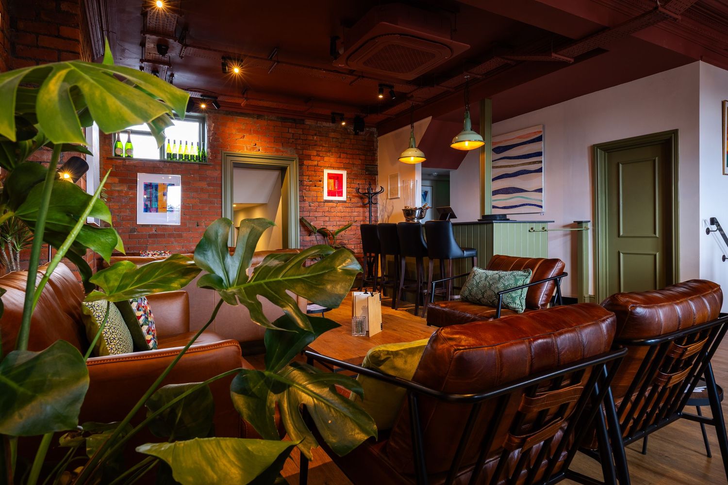 Warm lounge interior with exposed brick, leather seating, and lush greenery creating a cozy, modern atmosphere.