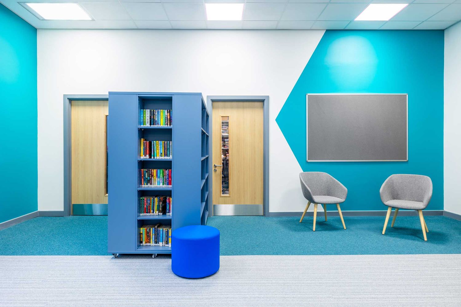 Modern school library or learning space with blue shelving, books, soft seating, and teal accent walls in a bright, contemporary interior.