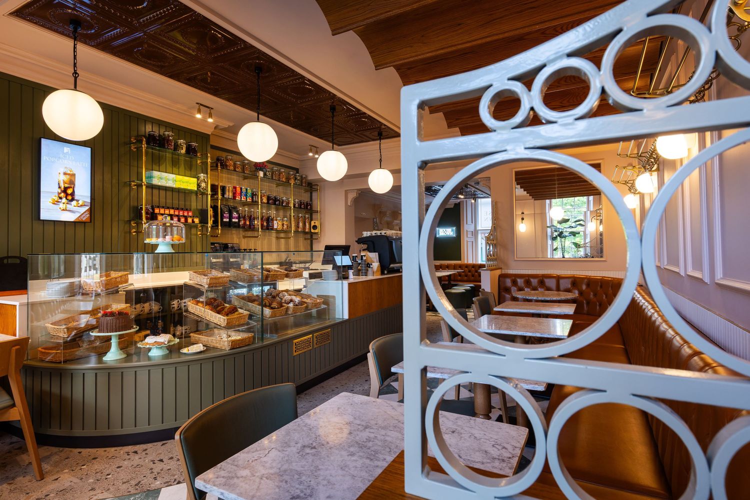 Cozy café interior with warm lighting, a pastry display, and stylish seating, viewed through a decorative circular room divider.