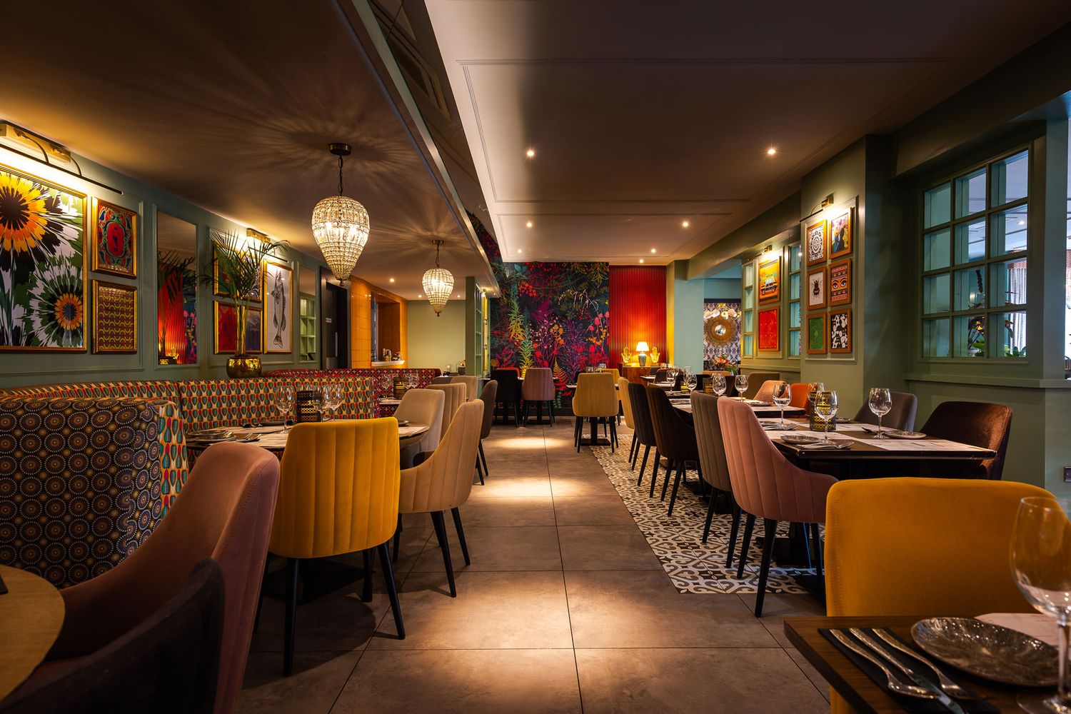 Vibrant dining space with colourful decor, patterned seating, crystal chandeliers, and a mix of modern and eclectic artistic details.