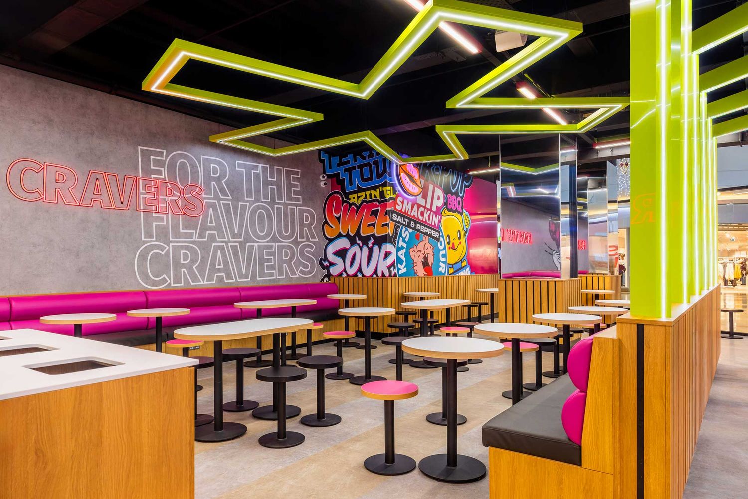 Vibrant fast-casual restaurant interior with neon ceiling lights, pink seating, bold wall graphics, and modern communal tables.