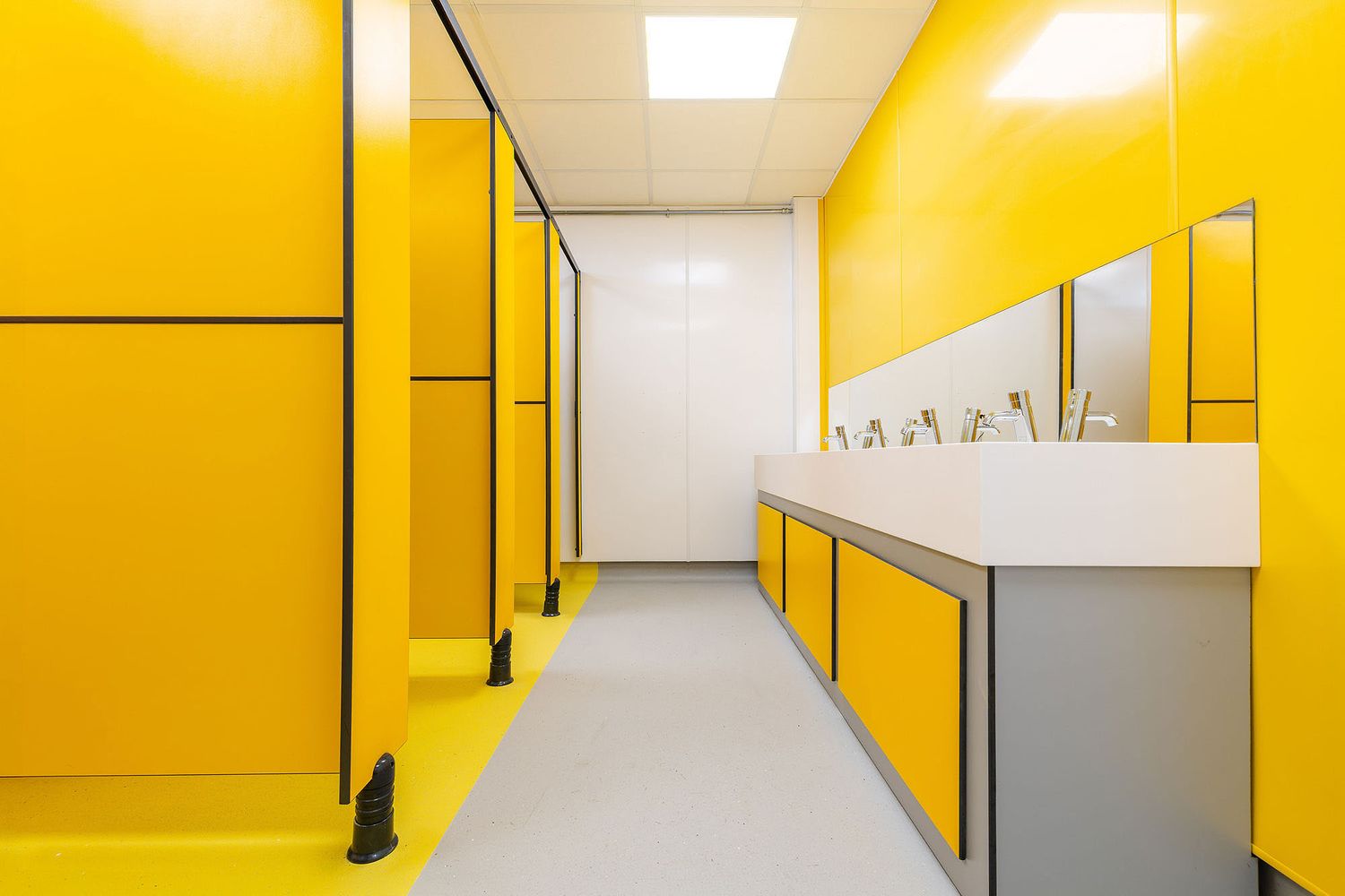 Bright yellow contemporary washroom interior with integrated sinks, mirrors and bold geometric wall panels.