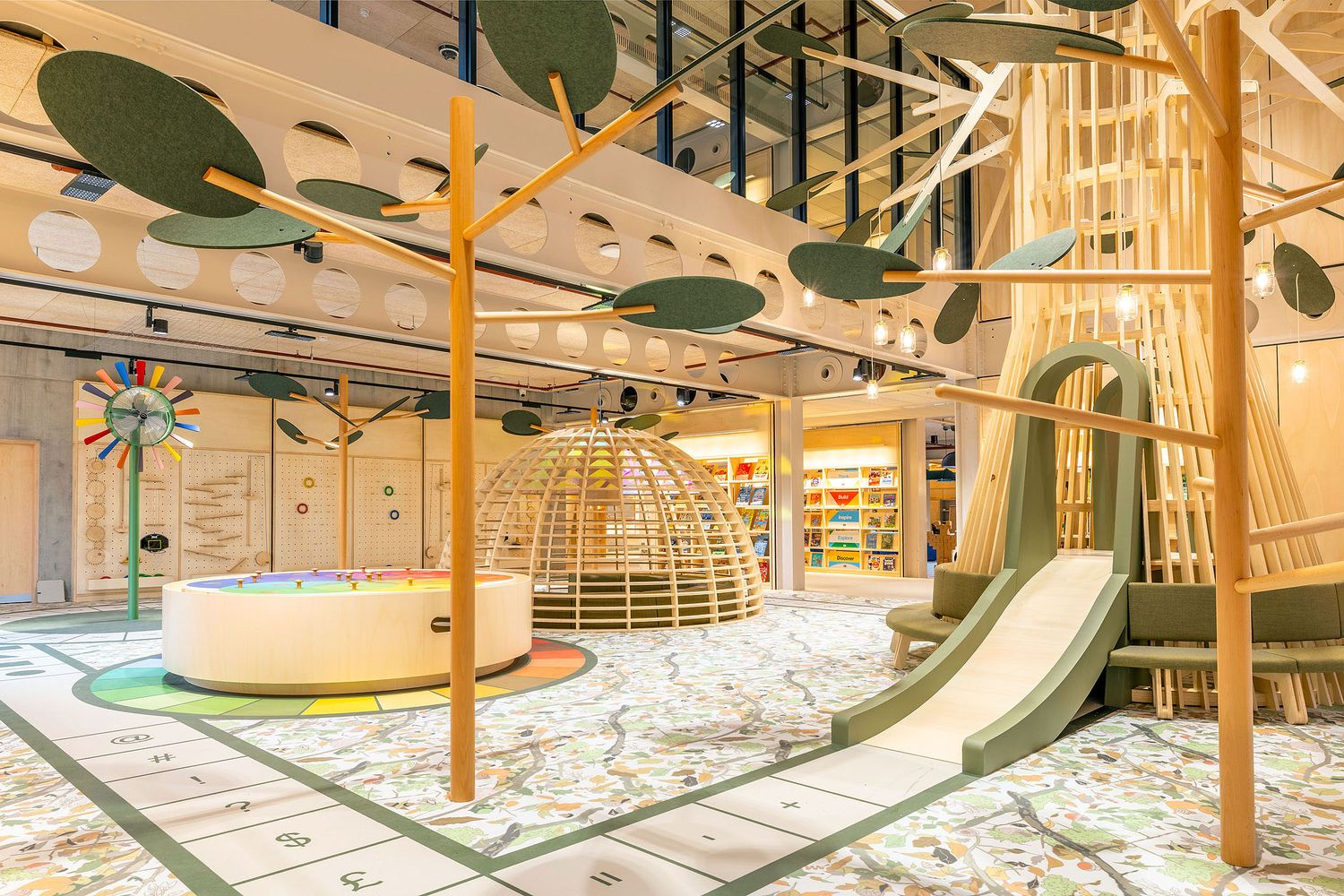 Children's library play area with bespoke wooden climbing structure, slide, interactive learning zones and contemporary interior design.