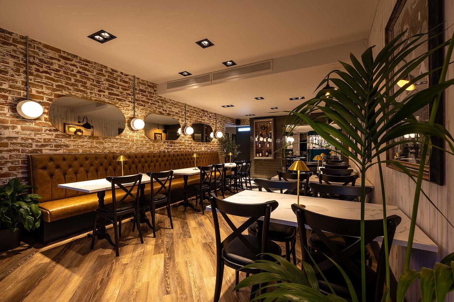 Elegant restaurant interior with warm lighting, exposed brick walls, marble tables and cosy booth seating in a stylish dining space.