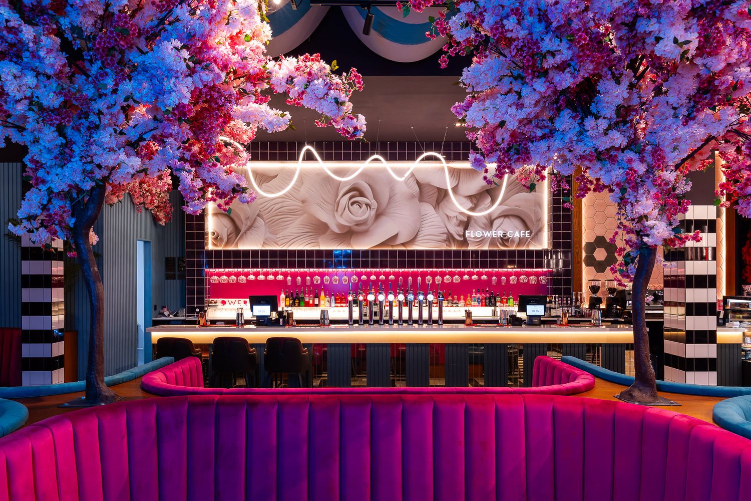Vibrant bar interior with pink blossom trees, bold lighting, and modern floral wall art at Flower Café.