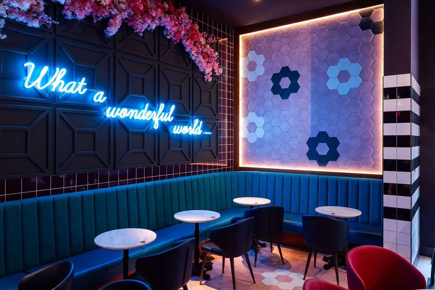 Vibrant café interior with blue neon sign, velvet seating, floral decor, and geometric tiled walls in a stylish modern design.